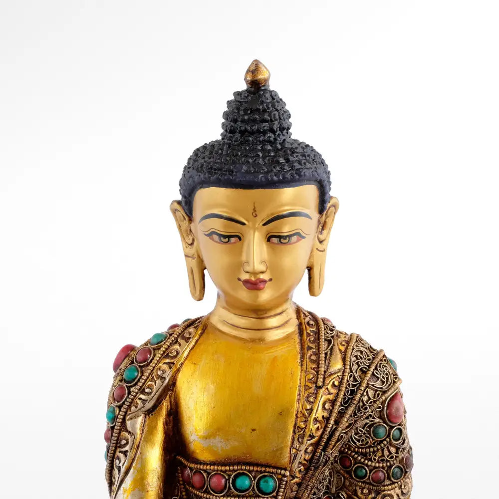 Vergoldete Buddha-Statue mit geschmücktem Gewand. Sein Gesichtsausdruck zeigt eine meditative friedliche Stimmung.
