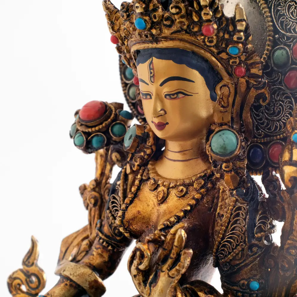 Das Gesicht der Weißen Tara ist in Gold gefasst. Sie hat ein drittes Auge auf ihrer Stirn. Ihre Krone und ihre Ohrringe sind mit Schmucksteinen besetzt.
