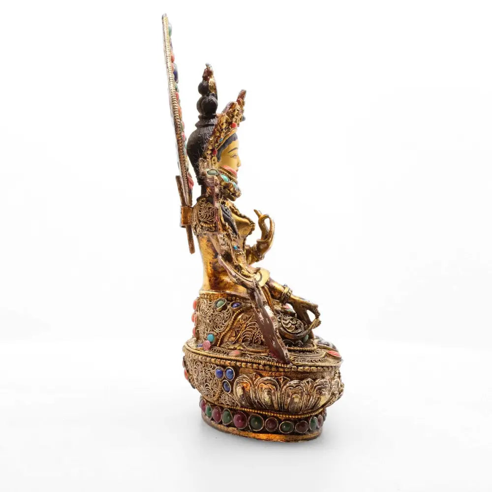 Profilansicht der Weißen Tara Statue. Ihr Gewand und der Lotusthron auf dem sie sitzt sind mit feinen Filigranornamenten verziert und mit farbigen Schmucksteinen besetzt.