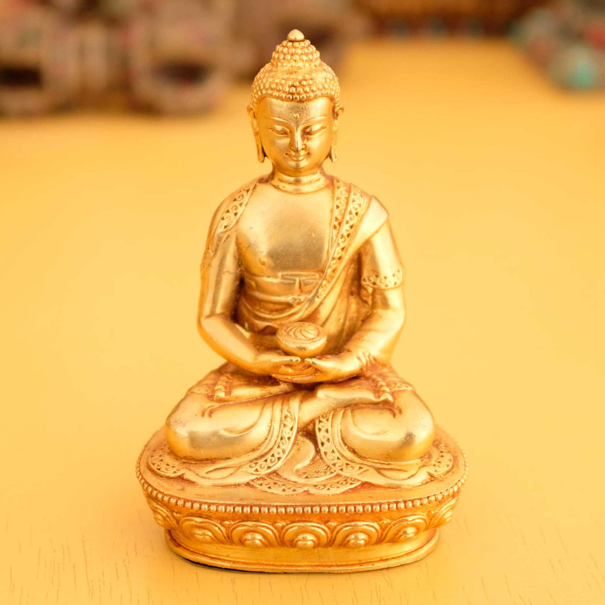 Kleine vergoldete Amitabha Buddha Statue, im Hintergrund rituelle Gegenstände des Vajrayana-Buddhismus in einer sanft beleuchteten Werkstattumgebung.