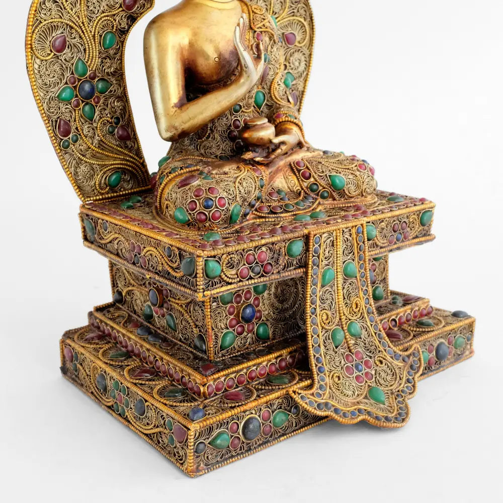 Amoghsiddhi Buddha Statue auf einem mehrstufigen Sockel, reich mit feinem Filigran verziert und farbigen Steinen akzentuiert.