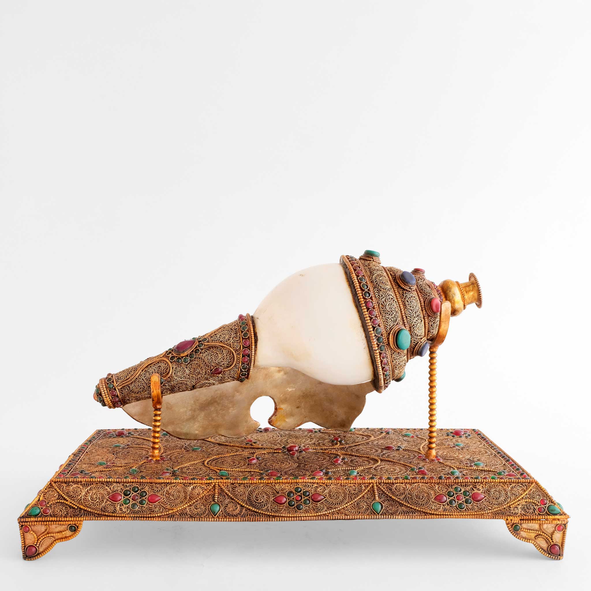 Rückansicht Shankha, Buddhistisches Muschelhorn, mit Filigran und geschnitzten Steinen verziert. Es ist versilbert und vergoldet. Auf einem einem Stand.