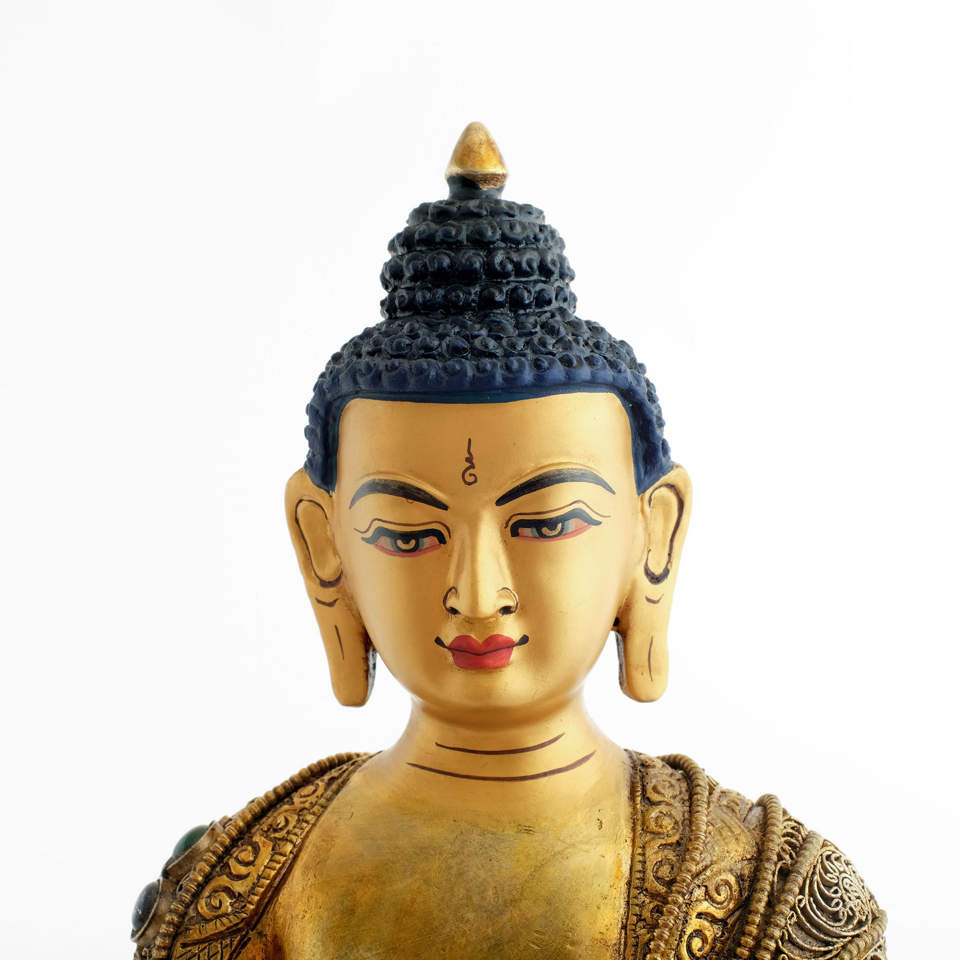 Das Gesicht der Shakyamuni Buddha Statue ist in Gold gefasst. An den langen Ohrläppchen, dem Schädelwulst (Ushnisha) und dem Stirnmal (Urna) kann man ablesen, dass der Buddha meditiert.