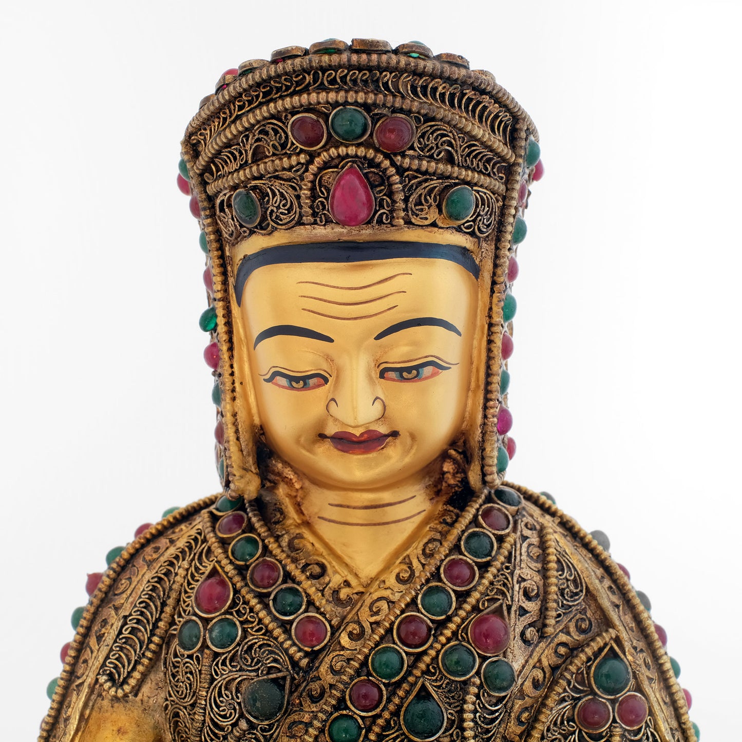 Detail der Gampopa Statue. Das Gesicht hat eine Kaltgold Bemalung. Er trägt den Hut der Kargyü Schule. Die Statue ist mit roten und grünen Steinen besetzt.