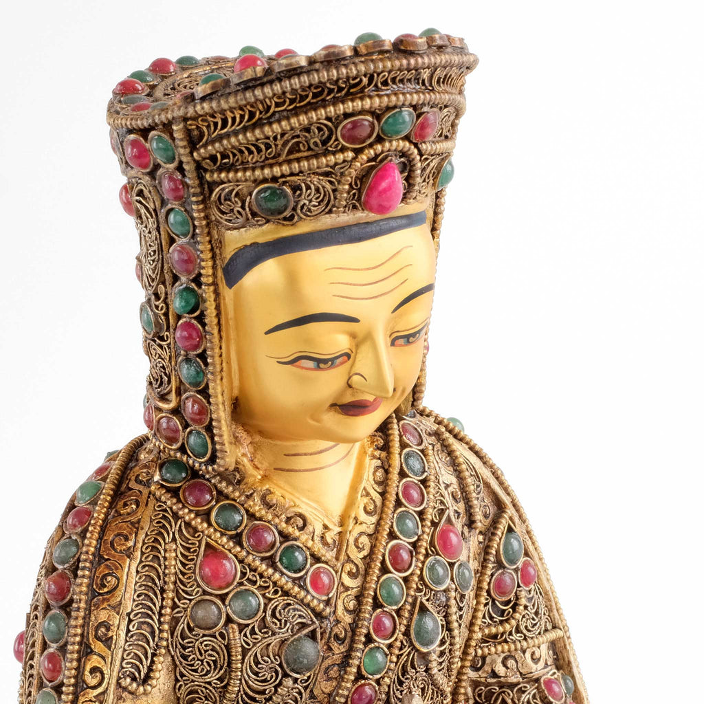 Detail der Gampopa Statue. Das Gesicht hat eine Kaltgold Bemalung. Er trägt den Hut der Kagyü Schule. Die Statue ist mit roten und grünen Steinen besetzt.