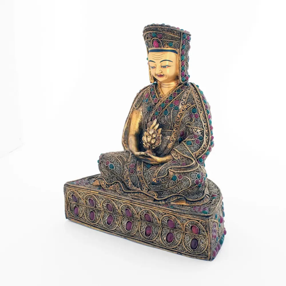 Gampopa Statue mit reich verzierter Robe und Sockel. Die Figur ist vergoldet, das Filigran ist versilbert und vergoldet. Mit roten und grünen Steinen besetzt.