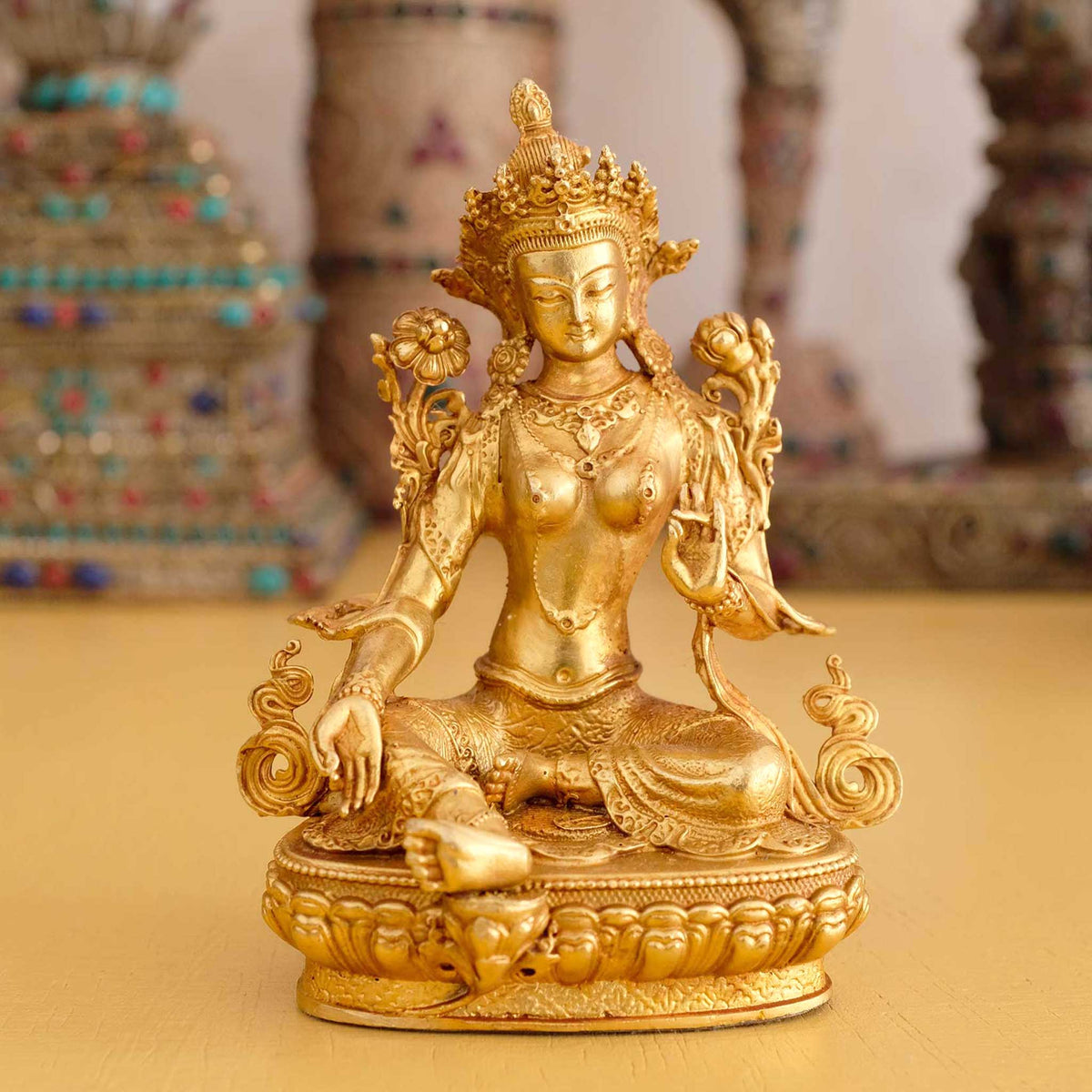 Kleine Grüne Tara Statue. Im Hintergrund rituelle Gegenstände des Vajrayana-Buddhismus in einer sanft beleuchteten Werkstattumgebung.