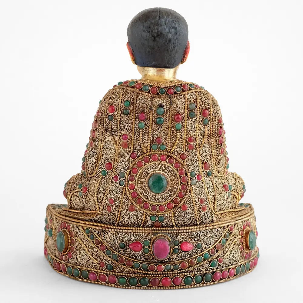Rückansicht der reich verzierten Guru Marpa Statue. Seine Robe ist verziert mit versilberten Filigranelementen die von vergoldetem Perldraht umrandet sind. Rote und Grüne Steine bilden farbige Bordüren und florale Ornamente.