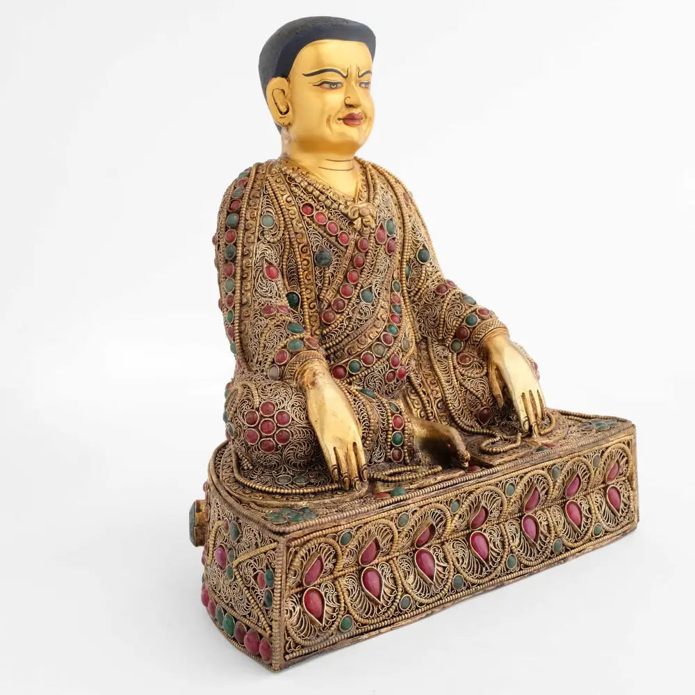 Guru Marpa, der Übersetzer. Er sitzt aufrecht auf einem halbrunden Sockel den vorn eine doppelte Reihe von Blütenblätter ziert. Seine Hände berühren den Boden.