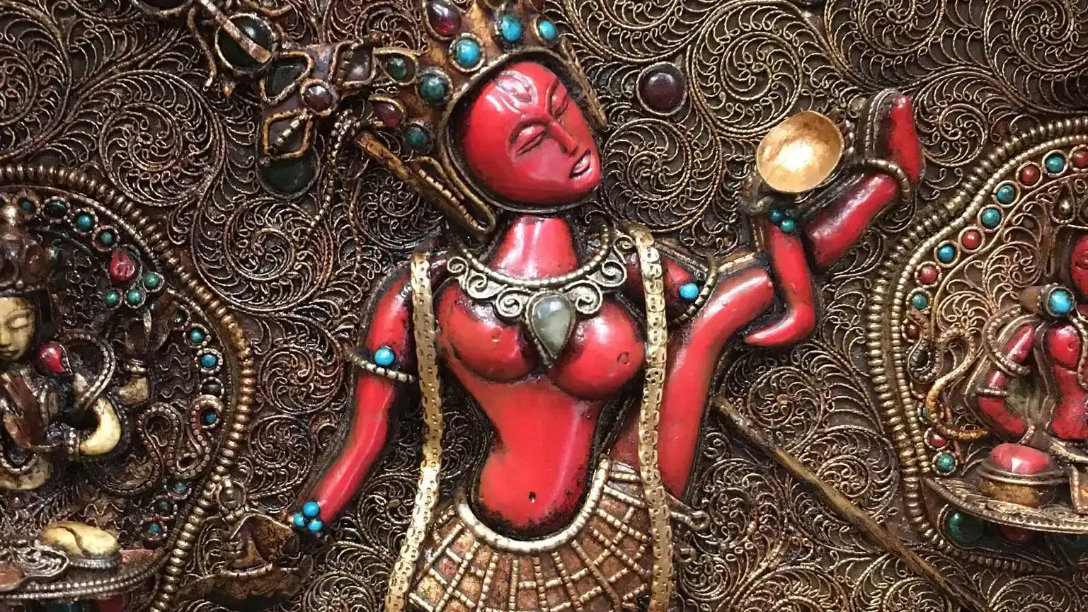 Handgeschnitzte rote Yogini, umgeben von anderen Gottheiten, auf einer filigranen Tafel.