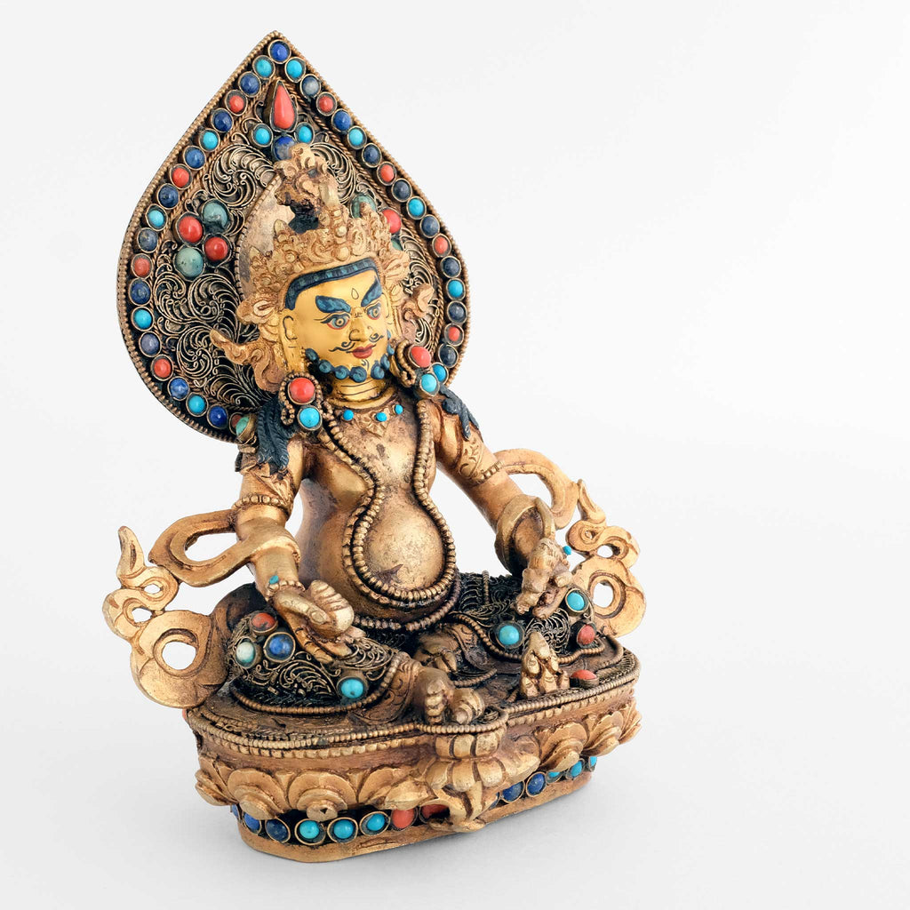 Seitenansicht Jambhala Statue. Er hält rechts eine Jambhara Frucht und links ein Nakula das Juwelen speit. Hinter seinem Kopf ist eine Aureole.