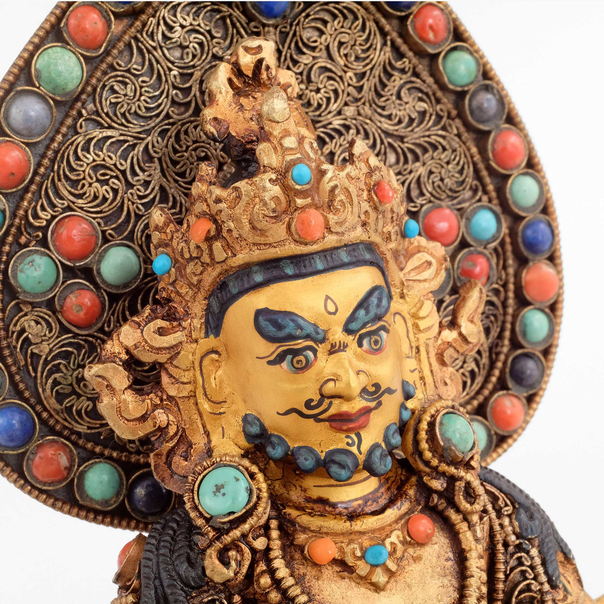Jambhala Statue mit Aureole. Detailaufnahme. Das Gesicht ist in Gold gefasst, die Aureole ist mit Filigran gestaltet und mit farbigen Steinen besetzt.