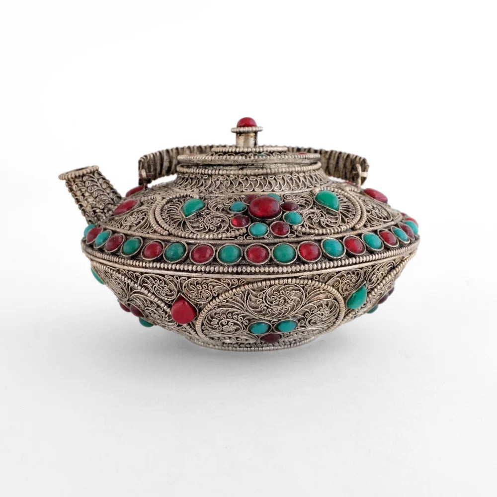 Verziertes versilbertes Kännchen mit roten und türkisfarbenen Steinen.