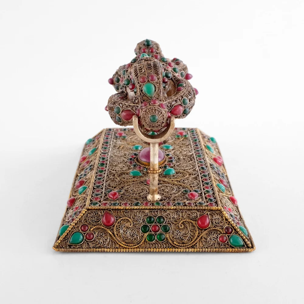 Der Vajra repräsentiert die unzerstörbare und diamantartige Natur der Erleuchtung. Er ist ein Symbol für grenzenlose Kraft. Die Oberflächen sind mit feinem versilberten Filigran verziert, die äußeren Linien aus Perlendraht sind vergoldet.