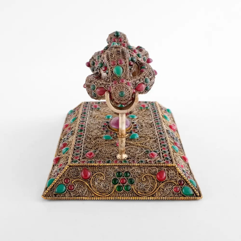 Der Vajra repräsentiert die unzerstörbare und diamantartige Natur der Erleuchtung. Er ist ein Symbol für grenzenlose Kraft. Die Oberflächen sind mit feinem versilberten Filigran verziert, die äußeren Linien aus Perlendraht sind vergoldet.
