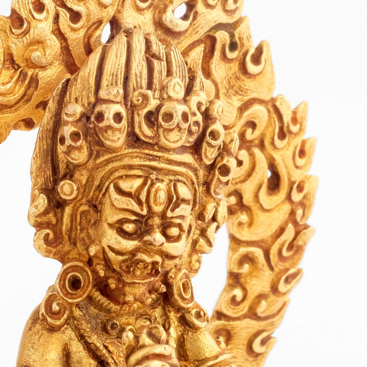 Small gold-plated Mahakala Statue. Close up of the head with skull crown. Detailed copper cast.