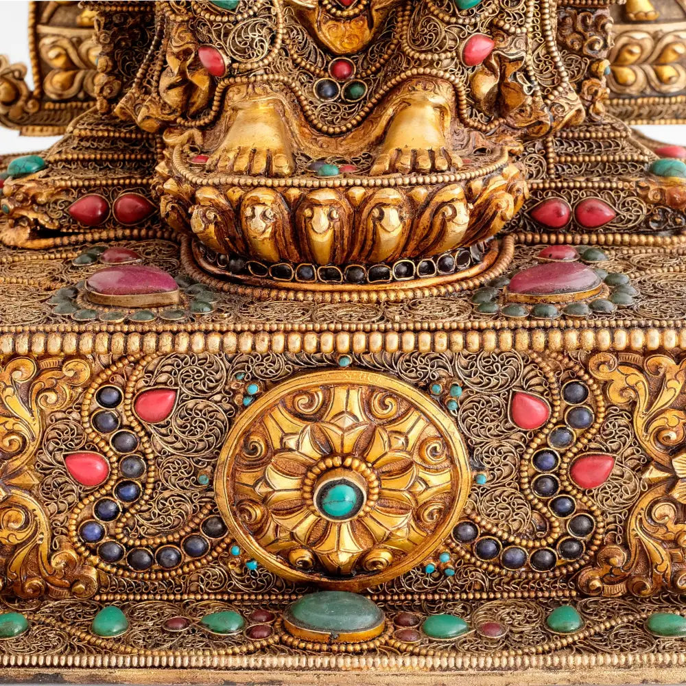 Die Füße des Maitreya Buddha sind auf einer Lotosblüte aufgesetzt. Sein Gewand ud Thron sind mit Filigran ud Repoussé verziert, versilbert und vergoldet. 
