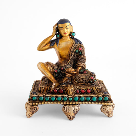 Milarepa statue, die Figur sitzt auf einem niedrigen Sockelthron. Der Tron und das Gazellenfell sind verziert mit feinem Filigran und mit farbigen Steinen besetzt.