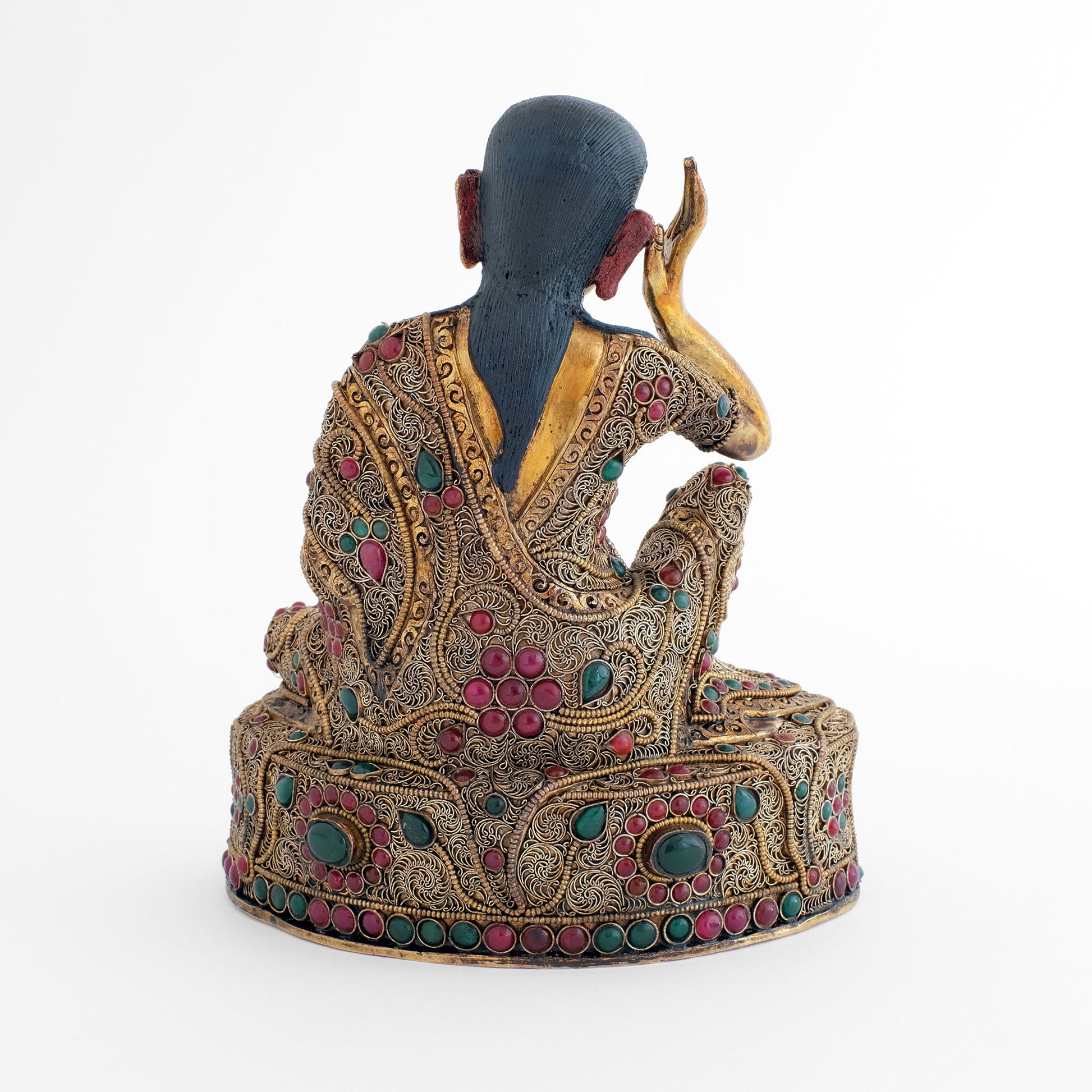 Rückansicht der Milarepa Statue. Das Gewand und der Thron auf dem er sitzt sind mit feinen floralen Filigran Elementen verziert. Das Filigran ist versilbert und vergoldet. Mit dunkelgrünen und dunkelroten Schmucksteinen akzentuiert.