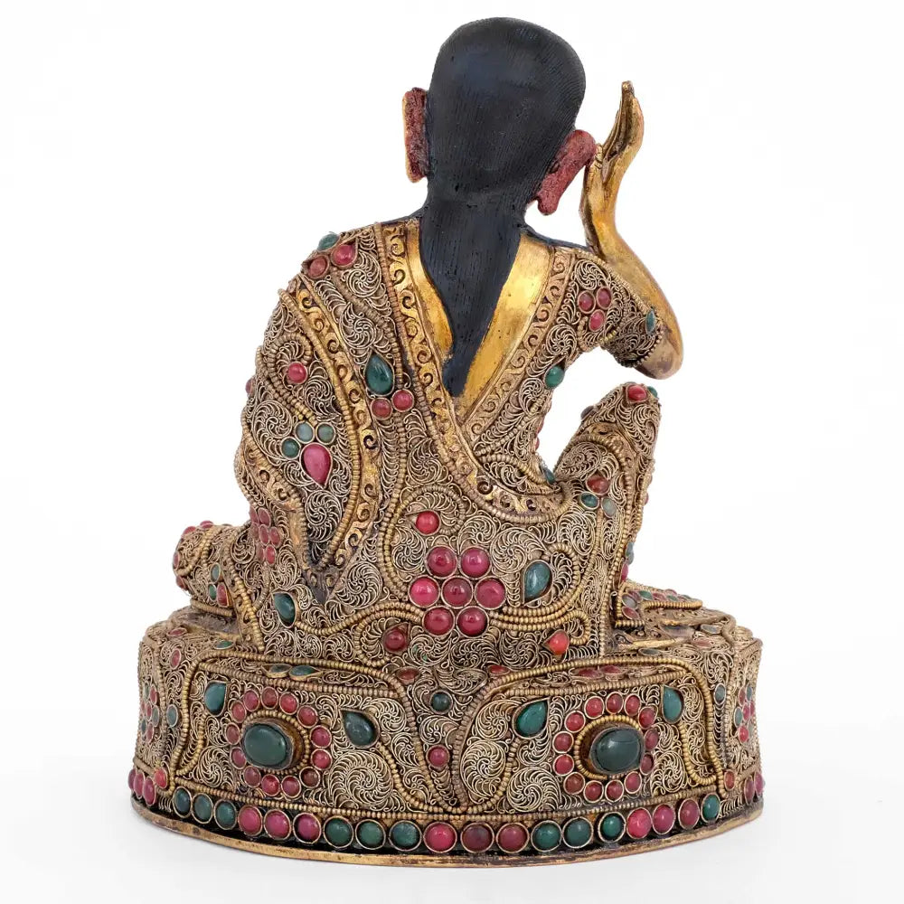 Rückansicht der Milarepa Statue. Das Gewand und der Thron auf dem er sitzt sind mit feinen floralen Filigran Elementen verziert. Das Filigran ist versilbert und vergoldet. Mit dunkelgrünen und dunkelroten Schmucksteinen akzentuiert.