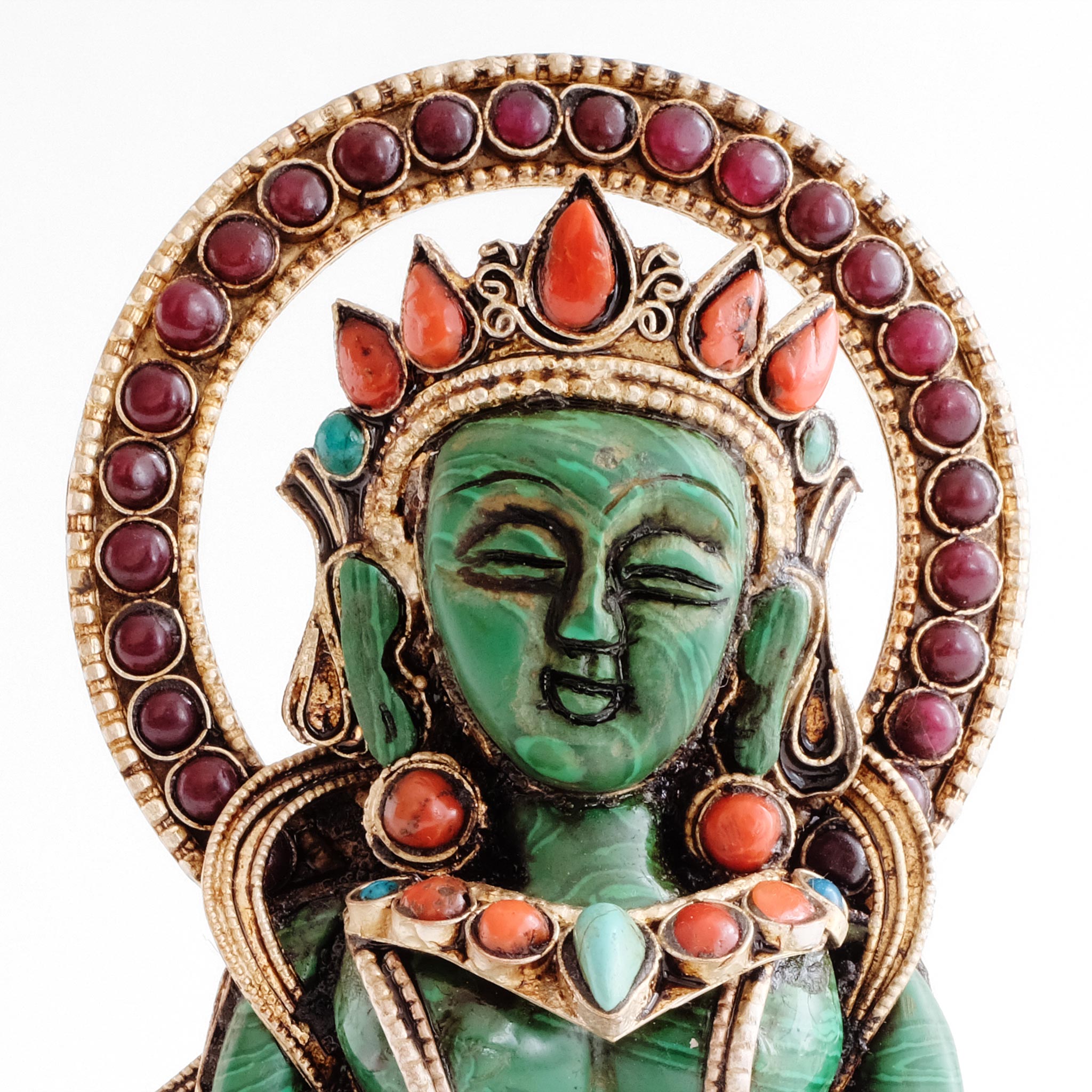 Nahaufnahme des Gesichts von Naga Kanya, aus grünem Stein geschnitzt, mit kreisförmiger Aureole und gefassten Steinen. 