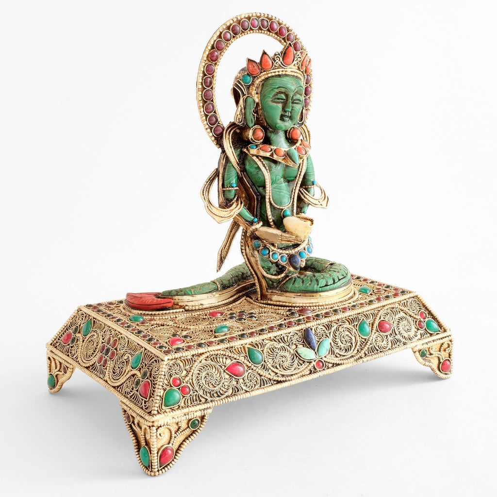 Seitenansicht der Naga Kanya Statue, die auf der rechten Hälfte eines rechteckigen filigranen Sockels sitzt.