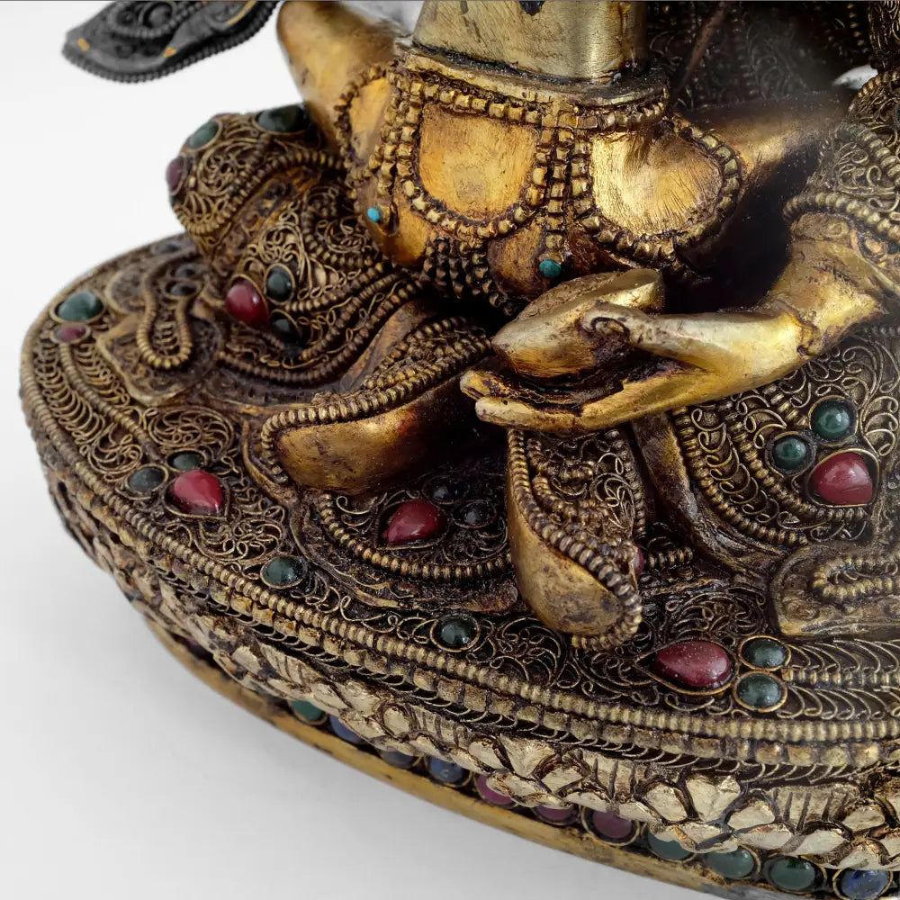 Padmasambhav trägt eine königliche Robe, sie ist mit feinen Filigran Elementen verziert und mit farbigen Steinen akzentuiert. Seine Gefährtin sitzt auf seinen abgewinkelten Beinen.