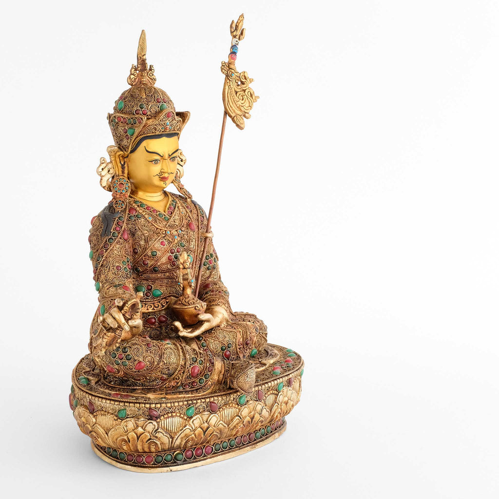 Padmasambhava, der Lotusgeborene, ist auch als Guru Rinpoche bekannt. Er sitzt in Lalitasana, seinen Stab Khatvanga an seiner linken Seite. In seiner linken Hand, die er in den Schoß legt, hält er eine Schädelschale, die rechte Hand ein vajra.