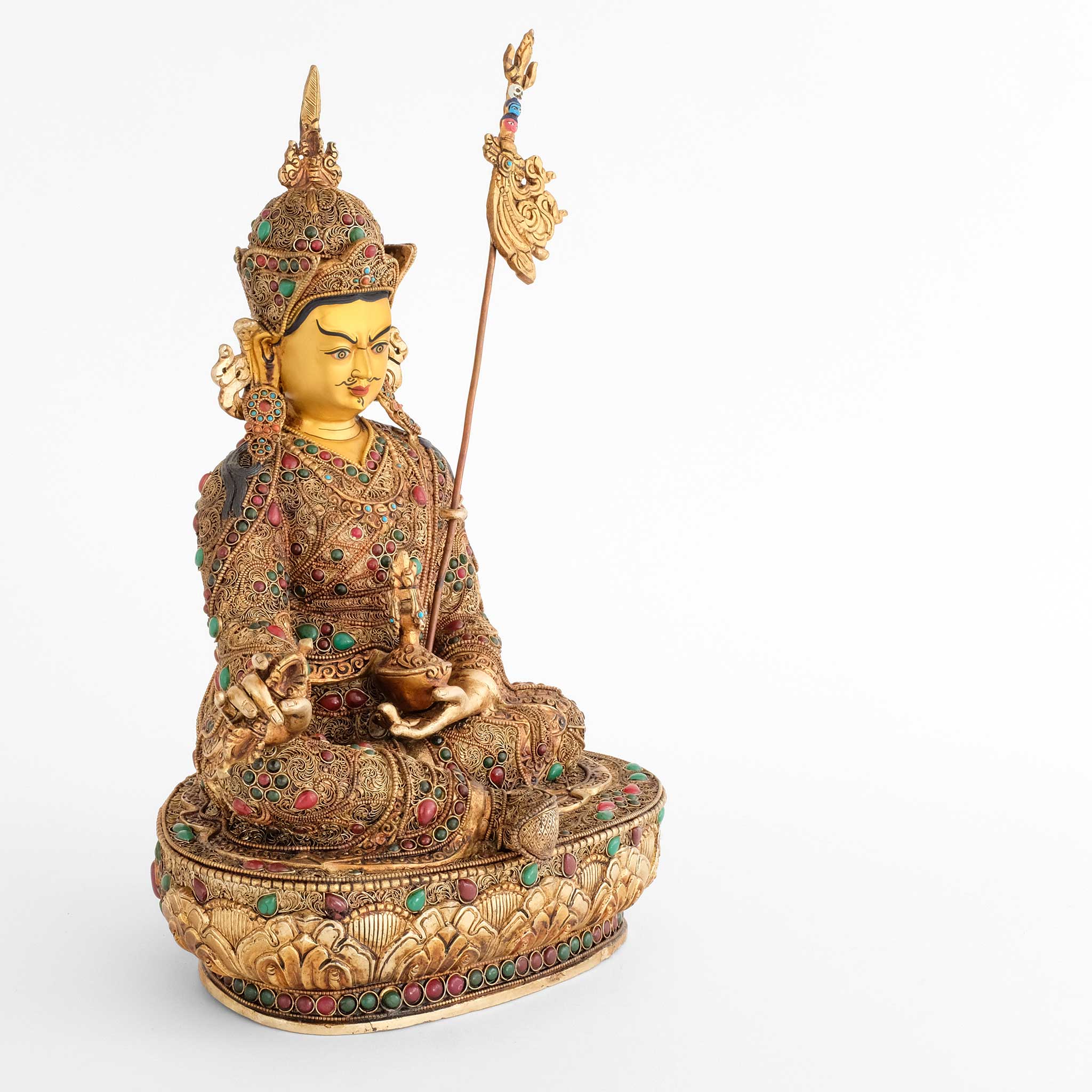 Padmasambhava, der Lotusgeborene, ist auch als Guru Rinpoche bekannt. Er sitzt in Lalitasana, seinen Stab Khatvanga an seiner linken Seite. In seiner linken Hand, die er in den Schoß legt, hält er eine Schädelschale, die rechte Hand ein vajra.