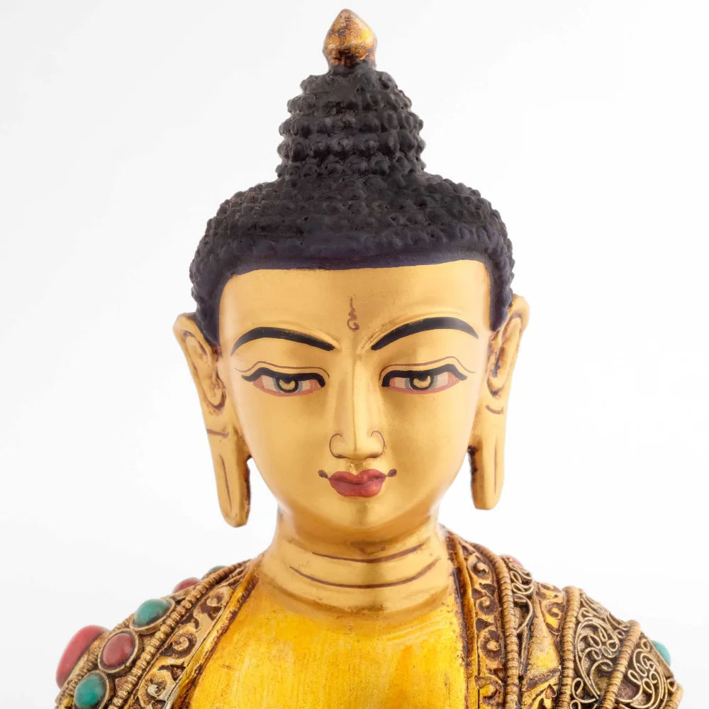 Vergoldete Buddha-Statue mit geschmücktem Gewand. Sein ebenmäßiges Gesicht zeigt einen meditativen friedlichen Ausdruck.