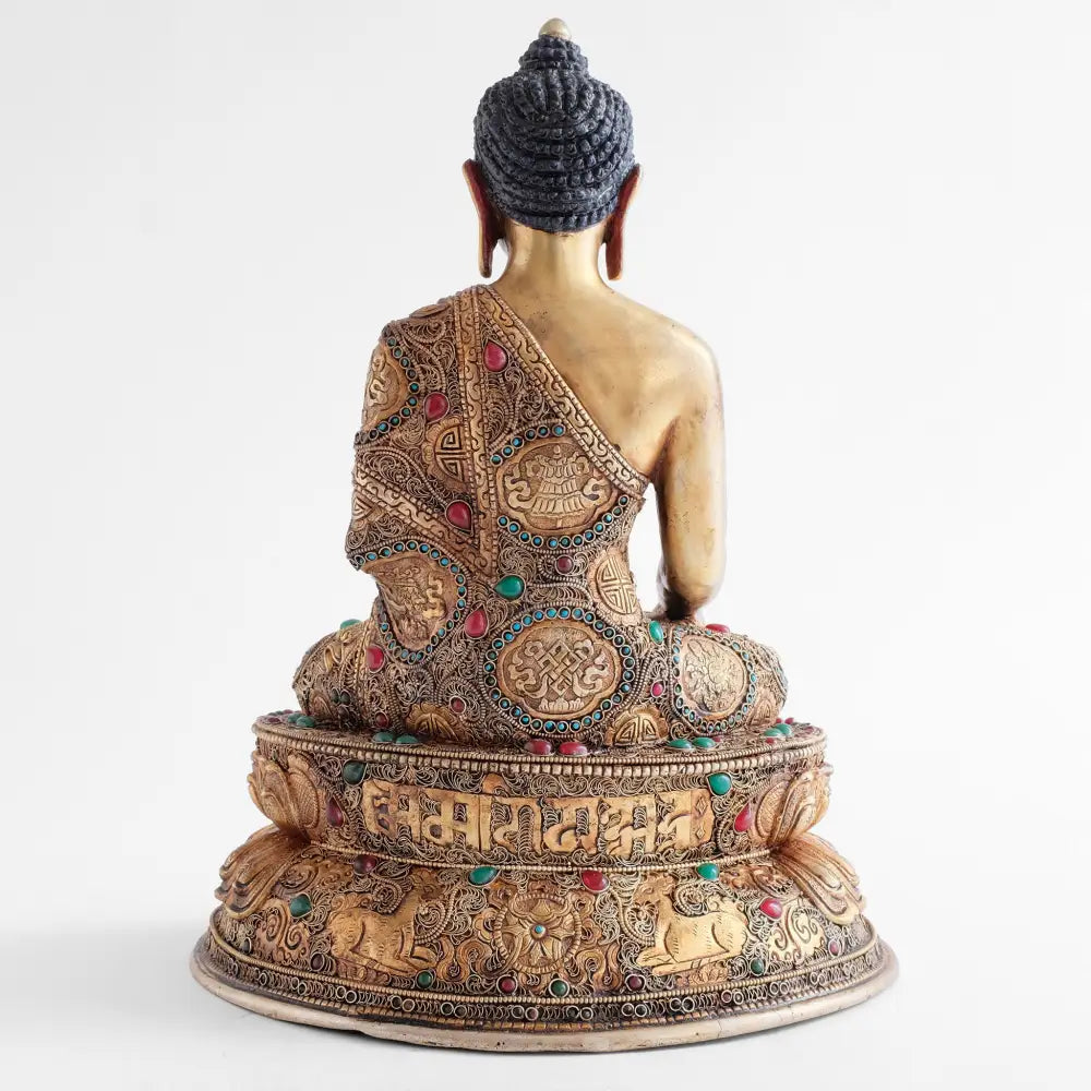 Die Rückseite der Shakyamuni Buddha Figur zeigt die reiche Verzierung seines Gewandes mit glücksverheißenden Symbolen, die von gefassten Türkissteinen und feinen Filigran Ornamenten umgeben sind.