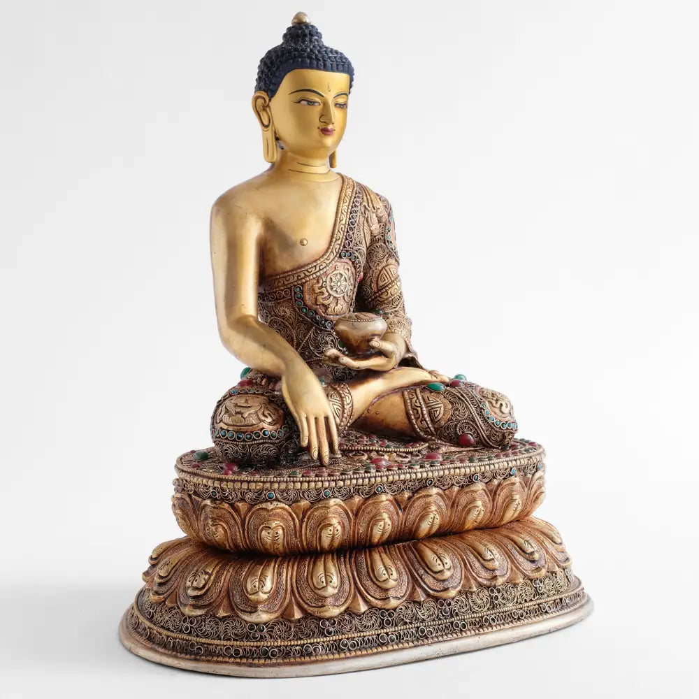 Gautama Buddha, Statue, sein Gewand ist mit filigranen Ornamenten geschmückt. Seine rechte Hand berührt die Erde in Bhumisparsha Mudra. Die Almosenschale, die flach auf der linken Hand im Schoß ruht, ist das Symbol des Mönchsführers.