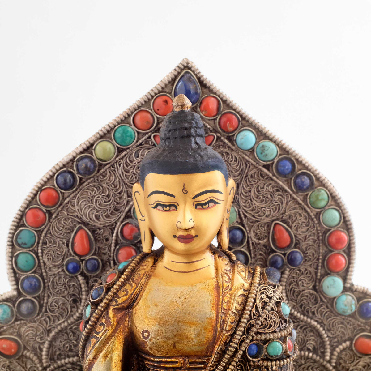 Shakyamuni Buddha Statue mit Aureole. Nahaufnahme des Gesichts. Der Hintergrund und sein Gewand sind mit Filigran gestaltet und Koralle, Lapis Lazuli und Türkis besetzt. 