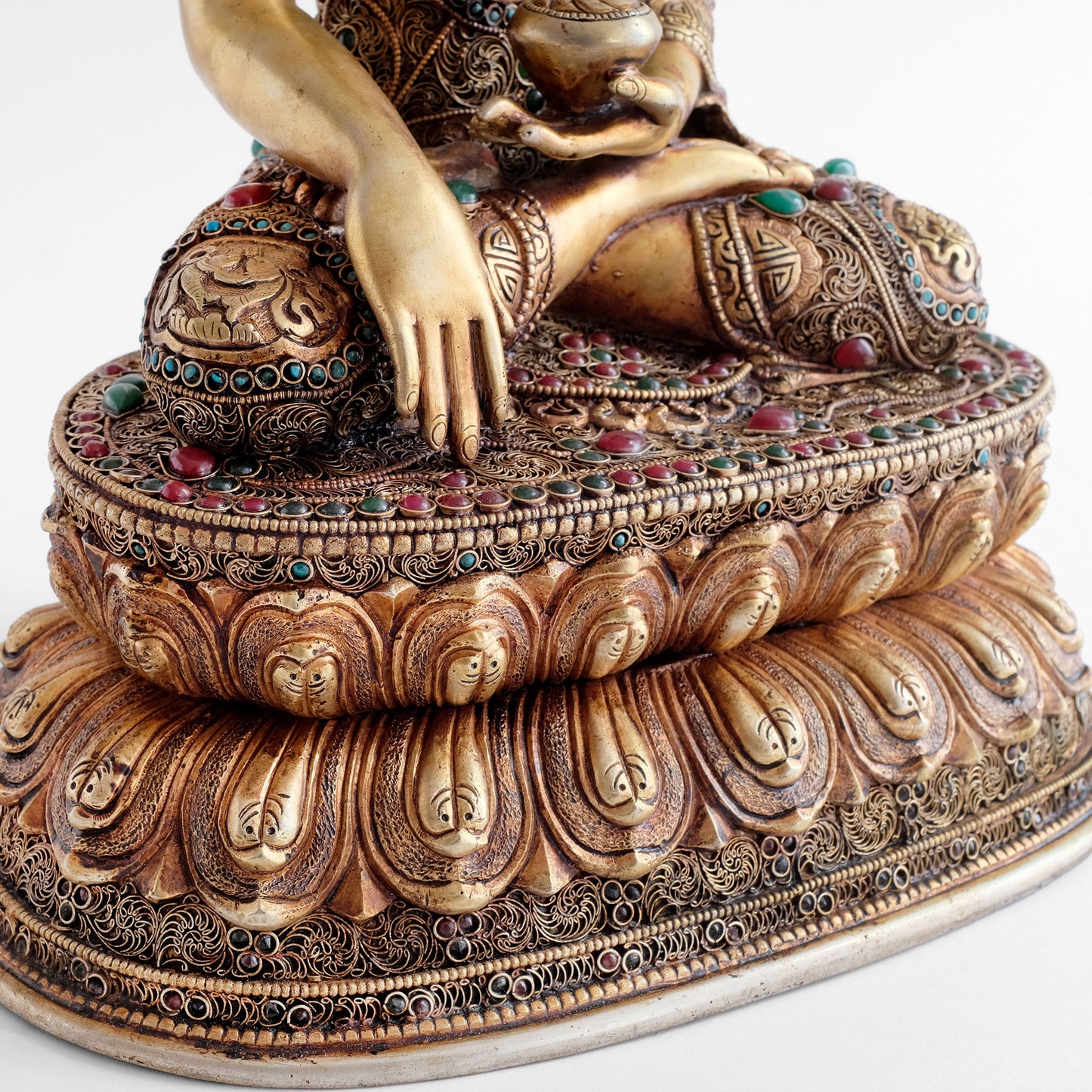 Gewand und doppelter Lotussockel der Siddhartha Gautama, Shakyamuni Buddha Statue sind mit feinen filigranen Ornamenten verziert und mit farbigen Steinen besetzt. Seine rechte Hand im erdberührenden, Bhumisparsha Mudra.