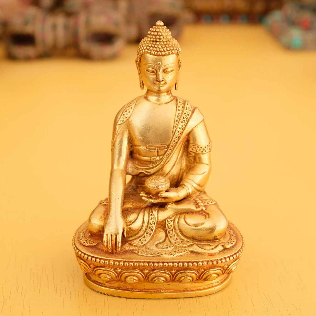 Kleine vergoldete Shakyamuni Buddha Statue im Hintergrund rituelle Gegenstände des Vajrayana-Buddhismus in einer sanft beleuchteten Werkstattumgebung.