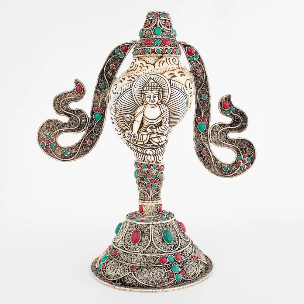 Tibetische Muscheltrompete, Shankha, in die Muschel ist das Bild von Bhaisajyaguru, dem Medizin Buddha geschnitzt, runder Kupferständer mit filigranen Verzierungen, versilbert, rote und grüne Steine.