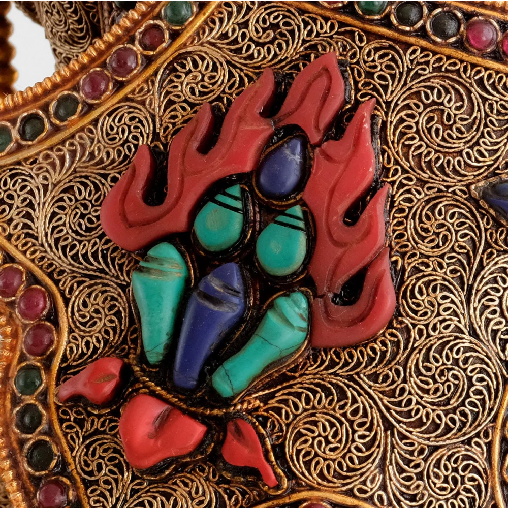 Versilberte spiralförmig angeordnete Filigranelemente und farbige Steine. Detail des geschnitzten Ratna, des Symbols des Dharma.