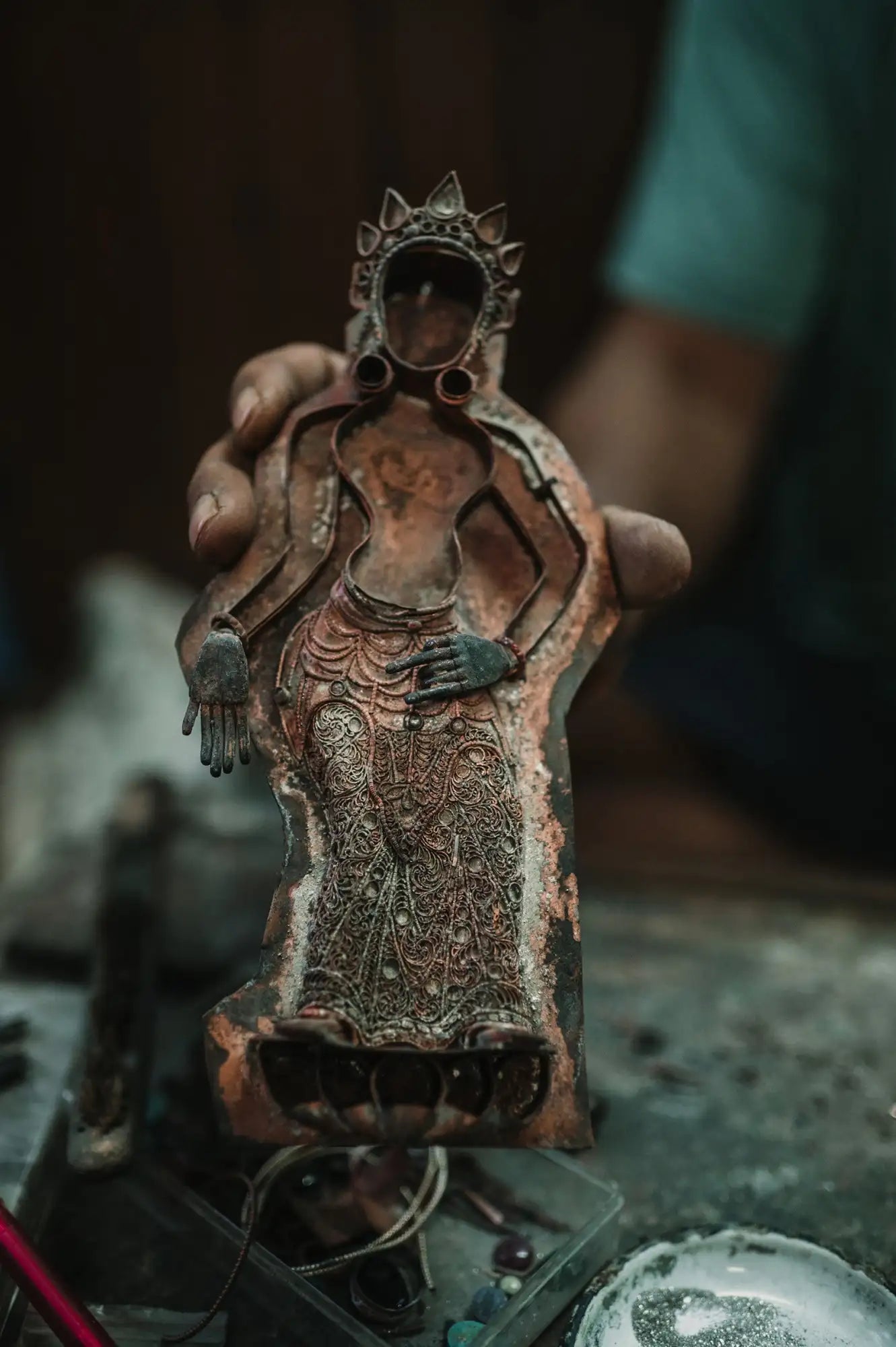 Shanta hält eine stehende Kupferfigur in der Hand. Die Robe der Figur ist mit Filigran Ornamenten geschmückt.