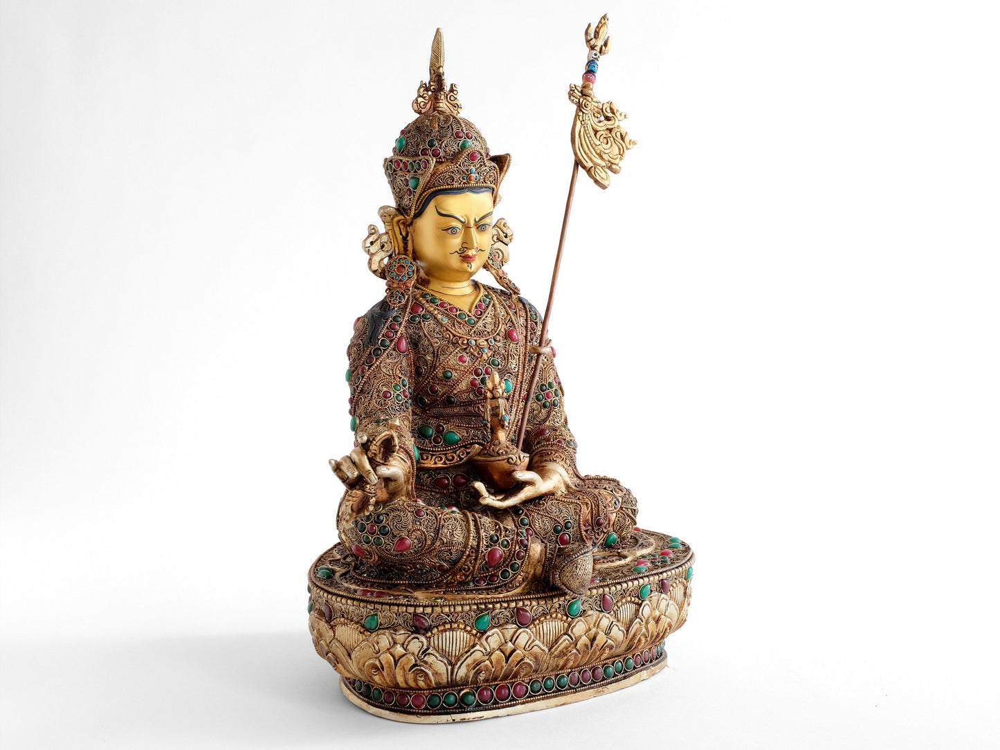 Padmasambhava, der Lotusgeborene, er ist auch als Guru Rinpoche bekannt. Er sitzt in Lalitasana, seinen Stab Khatvanga an seiner linken Seite. In seiner linken Hand, die er in den Schoß legt, hält er eine Schädelschale, mit der Langlebigkeits Vase Amrita.