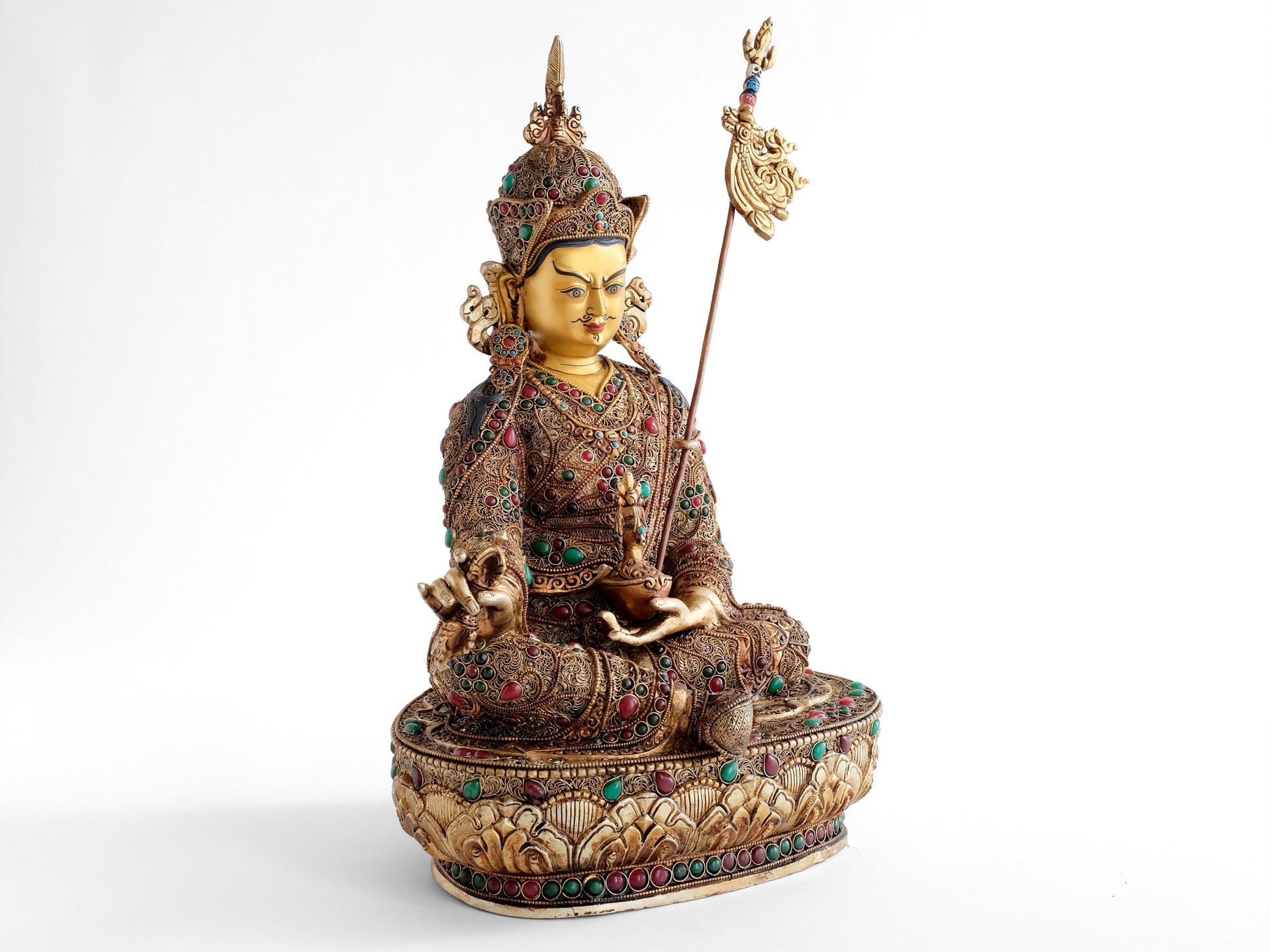 Padmasambhava, der Lotusgeborene, er ist auch als Guru Rinpoche bekannt. Er sitzt in Lalitasana, seinen Stab Khatvanga an seiner linken Seite. In seiner linken Hand, die er in den Schoß legt, hält er eine Schädelschale, mit der Langlebigkeits Vase Amrita.