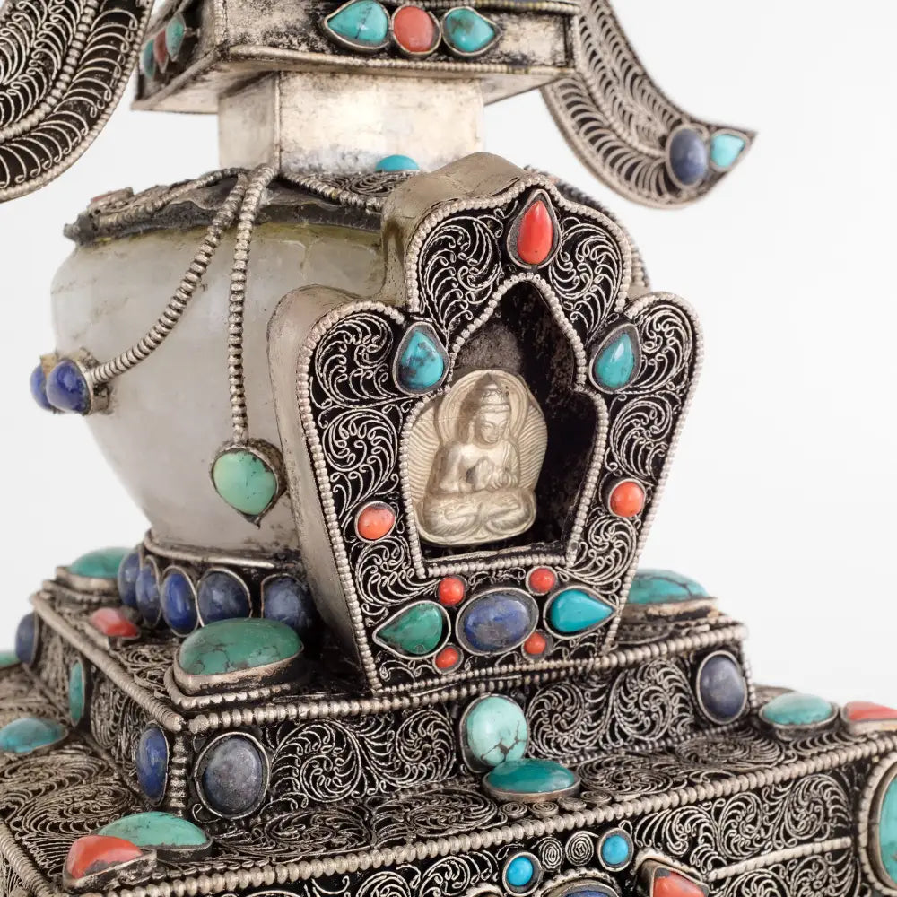 In der Gau-förmigen Vorderseite der Stupa befindet sich eine kleine geprägte Votivtafel aus Silber, die den Buddha Vairocana zeigt. Die Stupa, oder in tibetisch Chörten, ist mit Türkis, Lapislazuli und Koralle besetzt, die Kuppel ist aus Kristall.