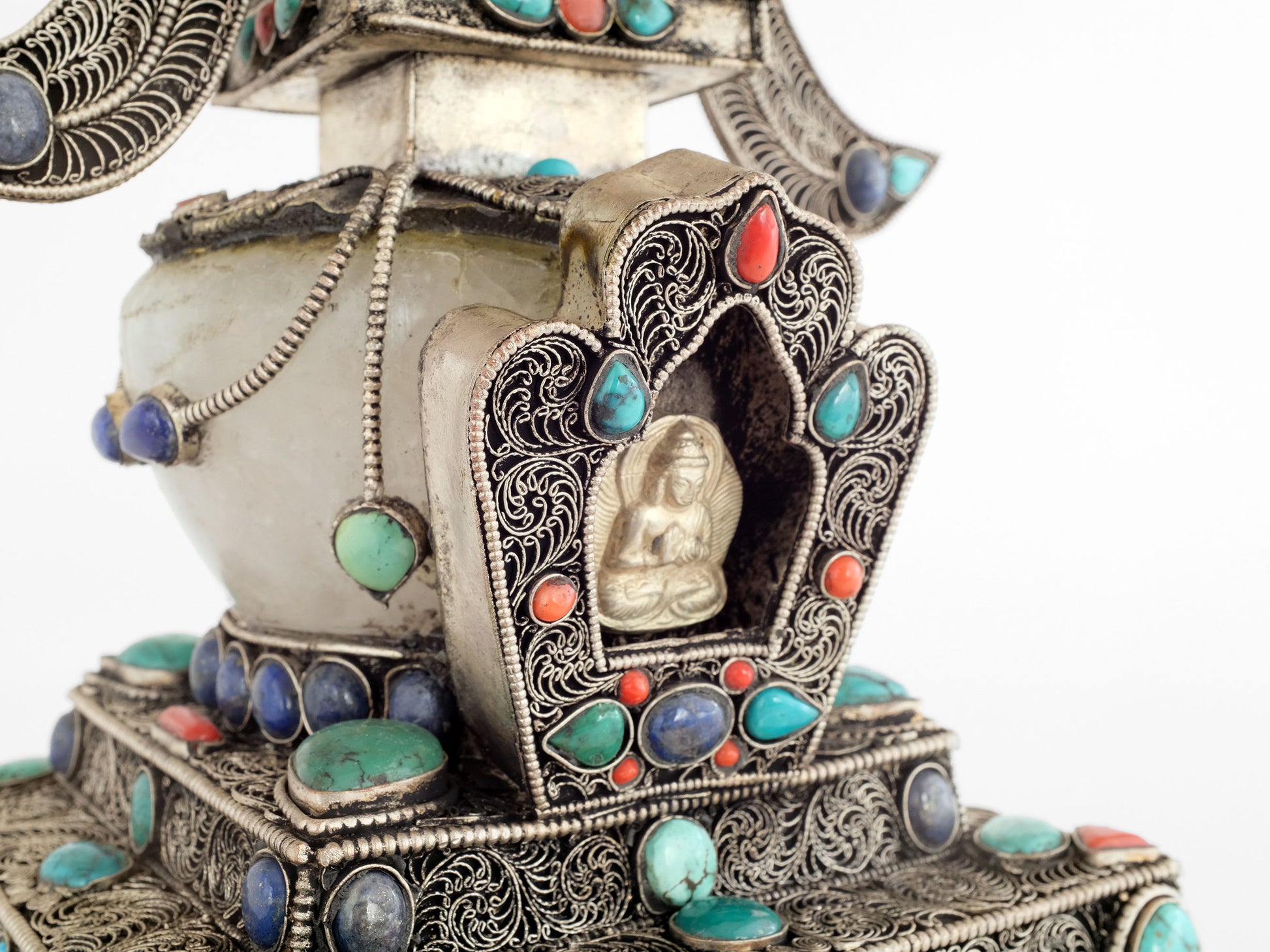 In der Gau-förmigen Vorderseite der Stupa befindet sich eine kleine geprägte Votivtafel aus Silber, die den Buddha Vairocana zeigt. Die Stupa, oder in tibetisch Chörten, ist mit Türkis, Lapislazuli und Koralle besetzt, die Kuppel ist aus Kristall.