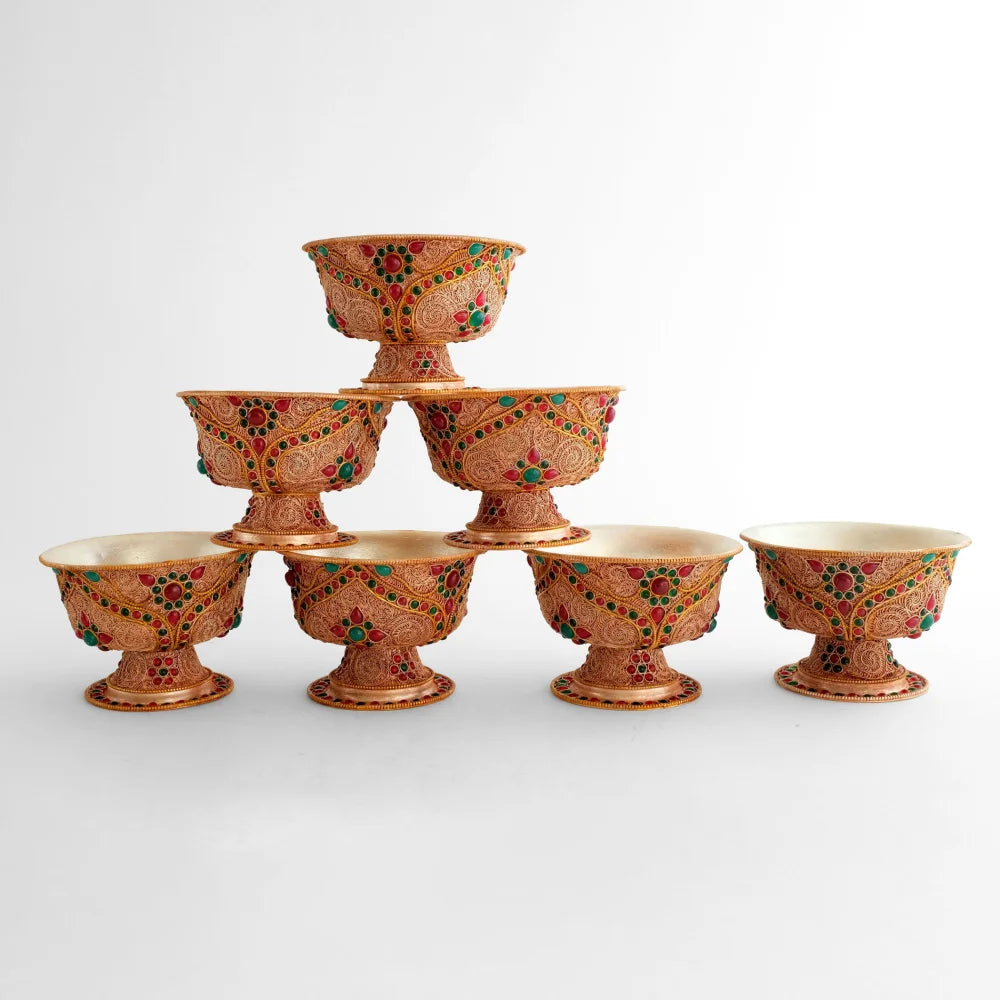 Ein Satz von sieben verzierten Sockelschalen für das buddhistische Wasseropfer Ritual. Sie sind aus Kupfer gefertigt und mit spiralförmigen Filigran Mustern verziert, mit roten und grünen Steinen akzentuiert.