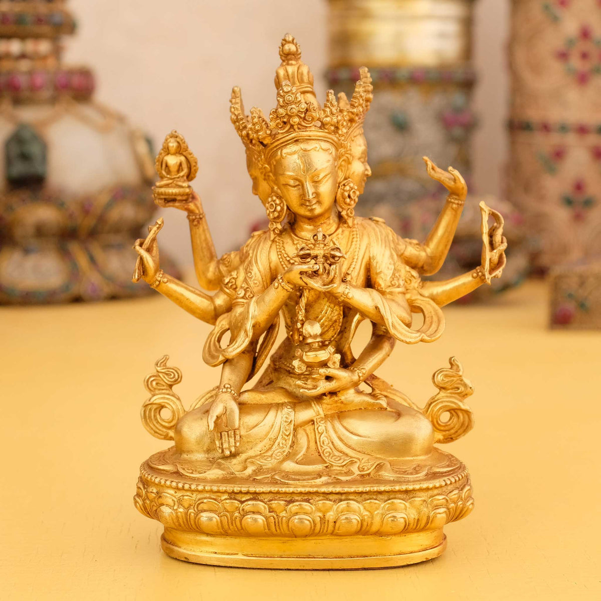 Kleine vergoldete Ushnishavijaya Statue, Namgyalma, im Hintergrund rituelle Gegenstände des Vajrayana-Buddhismus in einer sanft beleuchteten Werkstattumgebung.