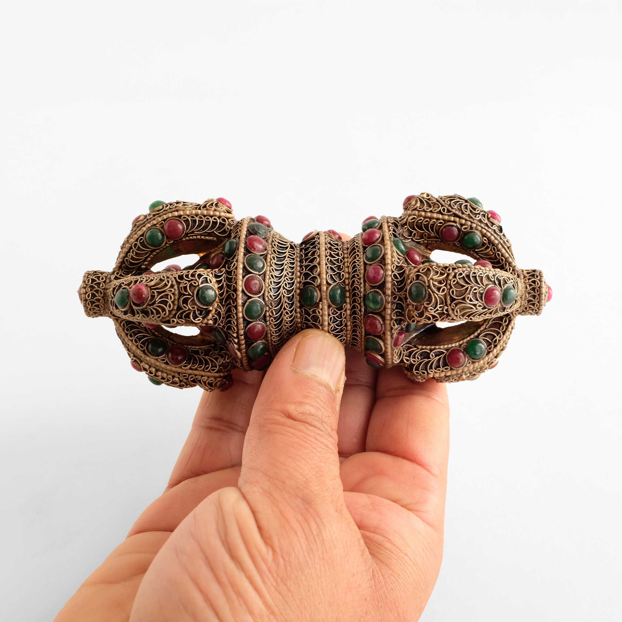 Verzierter Vajra aus Kristall mit roten und grünen Steinen. Gehalten von einer Hand für eine Größenreferenz.