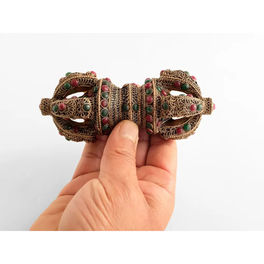 Verzierter Vajra aus Kristall mit roten und grünen Steinen. Gehalten von einer Hand für eine Größenreferenz.