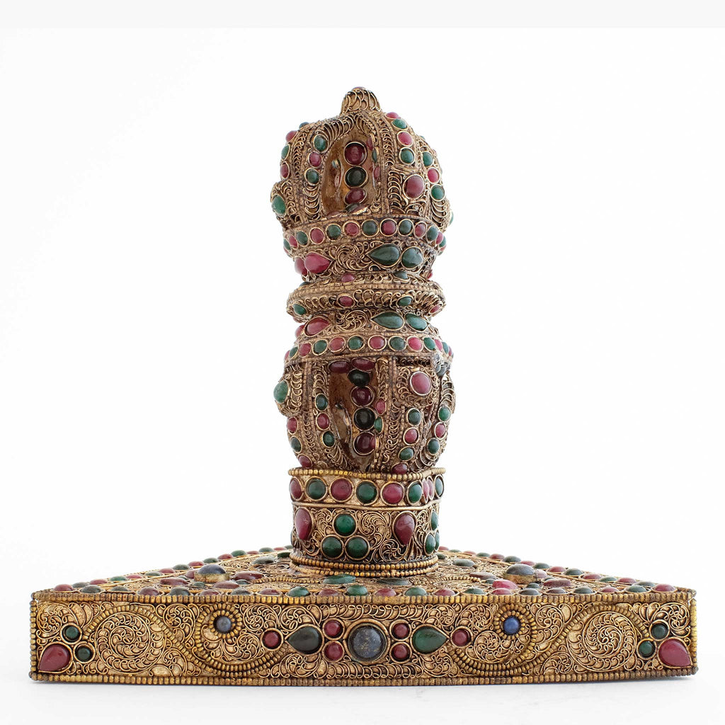 Vajra aus Kristall geschnitten auf einem dreieckigen Kupferstand, mit Filigran und farbigen Steinen.