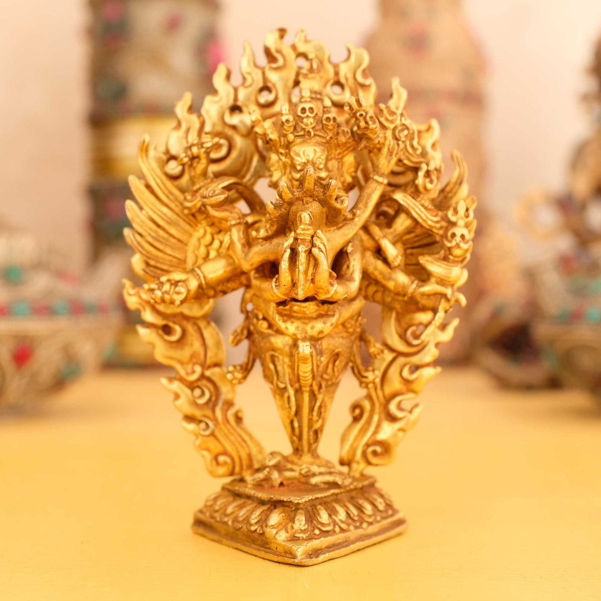 Kleine vergoldete Vajrakilaya Statue, Dorje Phurba, im Hintergrund rituelle Gegenstände des Vajrayana-Buddhismus in einer sanft beleuchteten Werkstattumgebung.