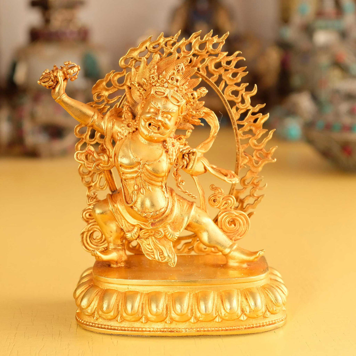 Kleine vergoldete Vajrapani Statue, im Hintergrund rituelle Gegenstände des Vajrayana-Buddhismus in einer sanft beleuchteten Werkstattumgebung.