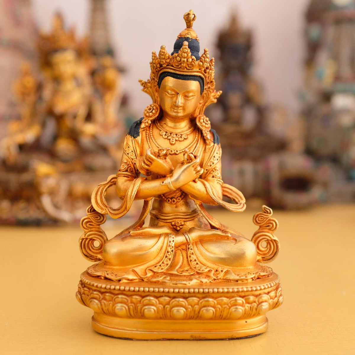 Kleine vergoldete Vajrasattva Figur, Dorje Sempa, im Hintergrund rituelle Gegenstände des Vajrayana-Buddhismus in einer sanft beleuchteten Werkstattumgebung.